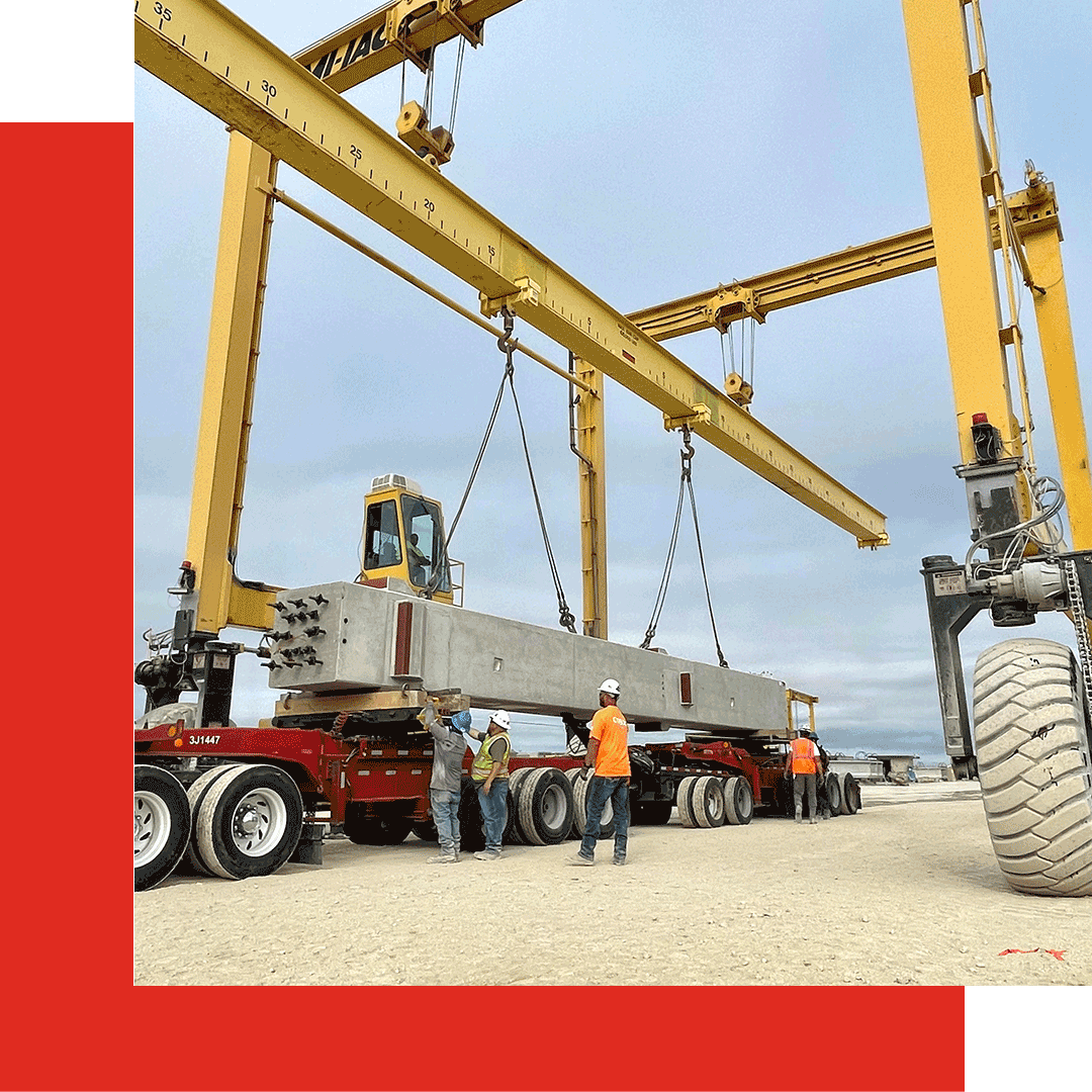 Workers guide a large concrete beam being lifted by a yellow crane onto a flatbed truck at a construction site. The sky is overcast. Red geometric shapes decorate the image's corner.