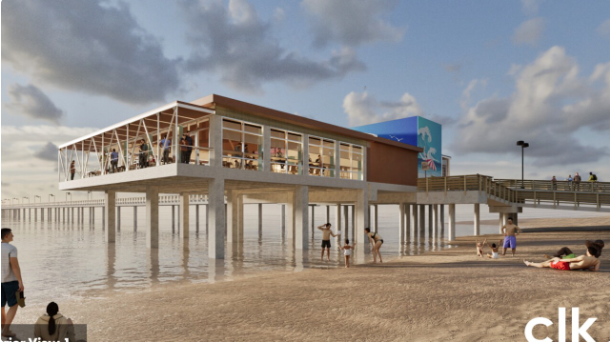 A modern pier structure with large windows extends over the ocean, supported by tall pillars. People walk and relax on the sandy beach below and along the pier under a partly cloudy sky.