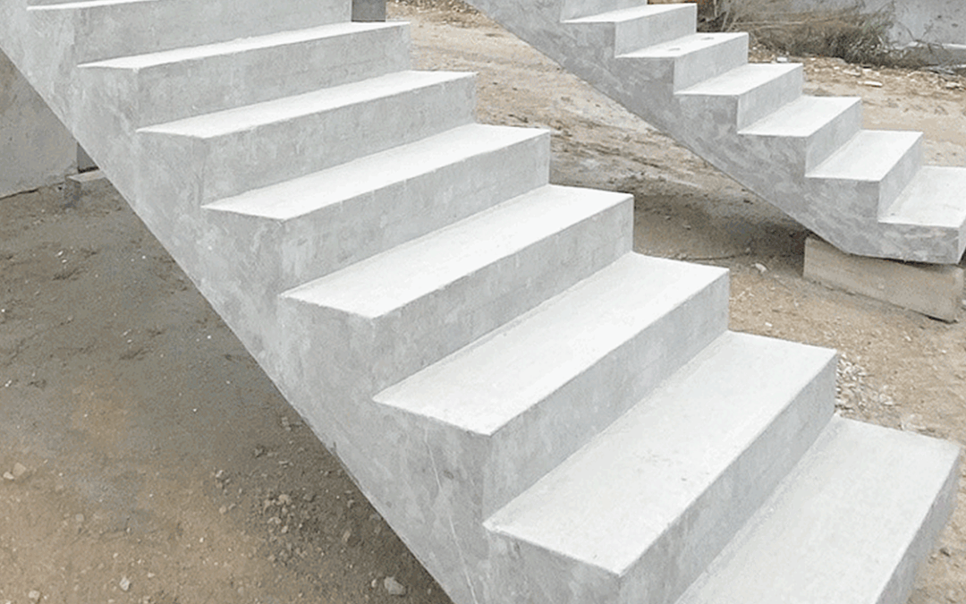 Two unfinished concrete staircases stand outdoors on a construction site with dirt ground; there are no railings, and construction materials and pipes are visible in the background.
